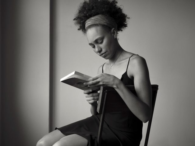 A black and white photograph of a your woman sitting in a chair and reading a book.