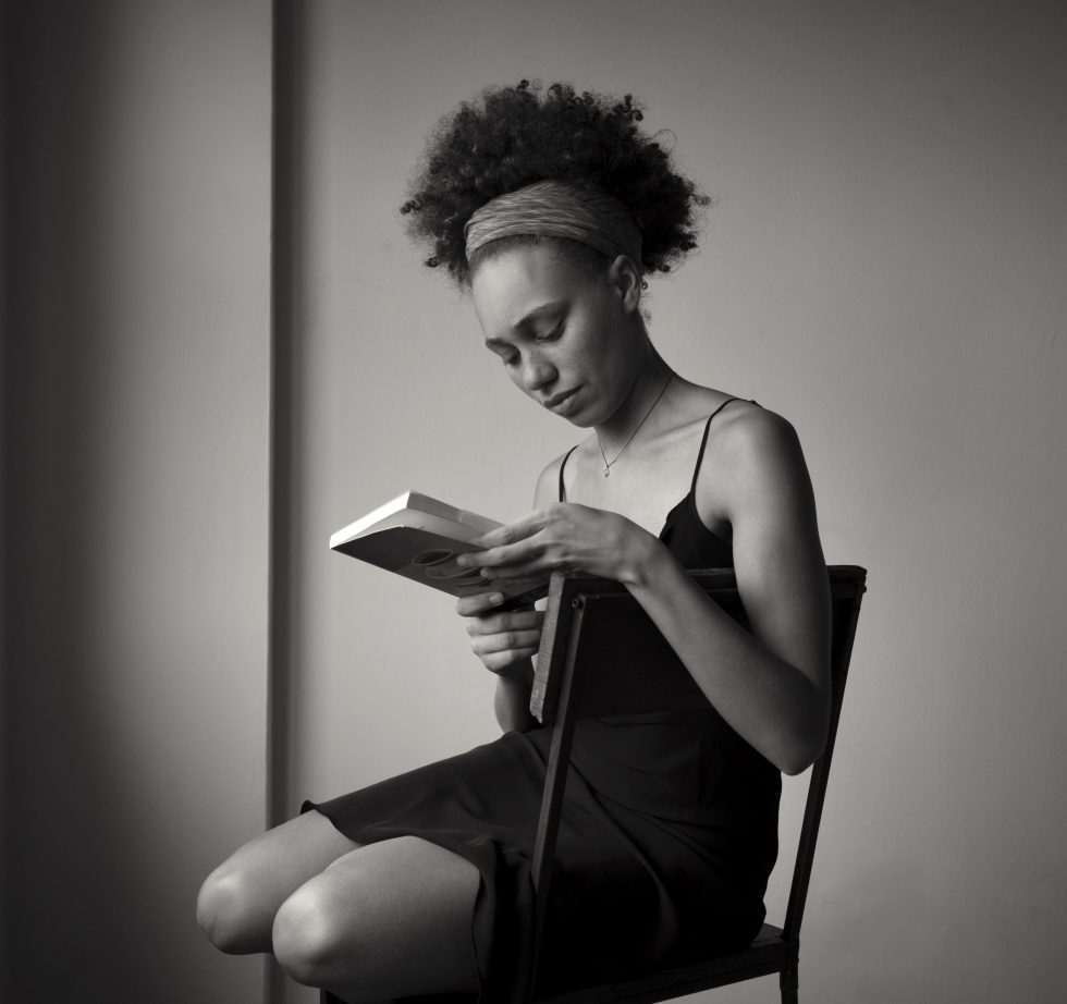 A black and white photograph of a your woman sitting in a chair and reading a book.