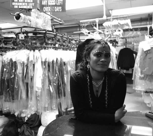 A black and white photograph of a woman in a dry cleaning store.