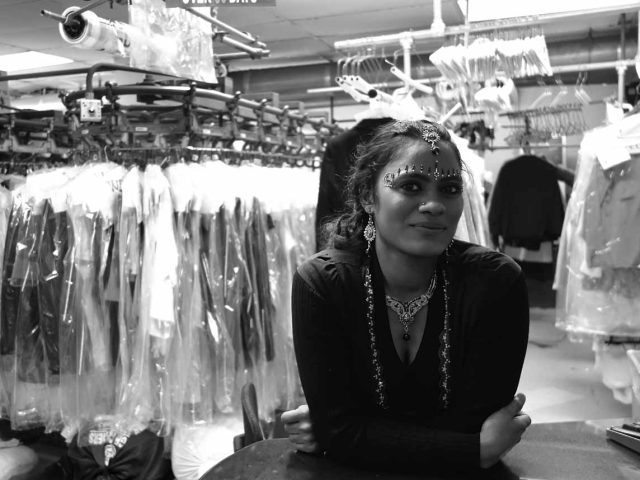 A black and white photograph of a woman in a dry cleaning store.
