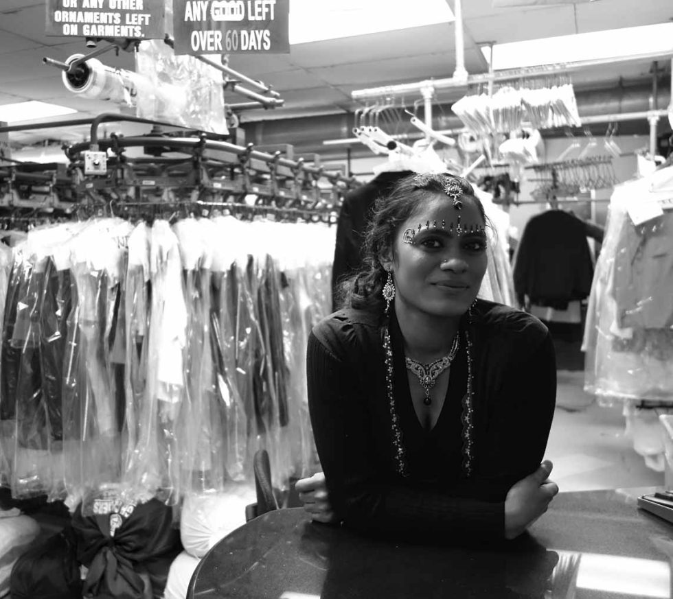 A black and white photograph of a woman in a dry cleaning store.