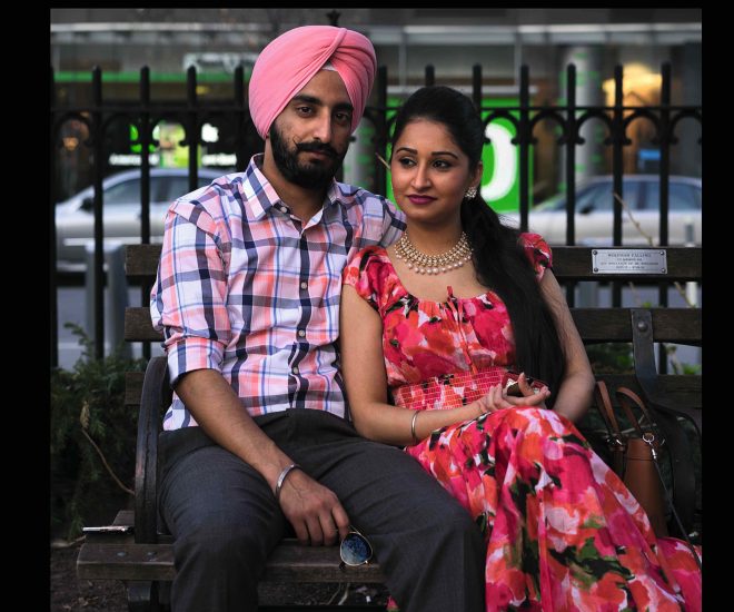 A photograph of a young couple sitting on a bench in a city park.