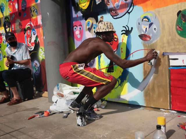 A photograph of an artist spray painting on a boarded-up building.