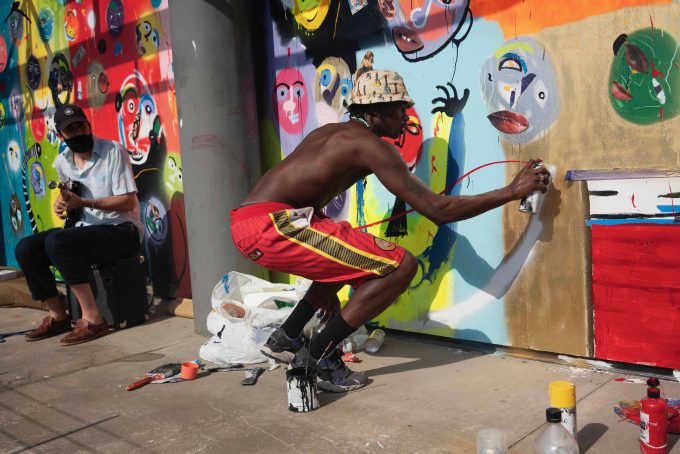 A photograph of an artist spray painting on a boarded-up building.
