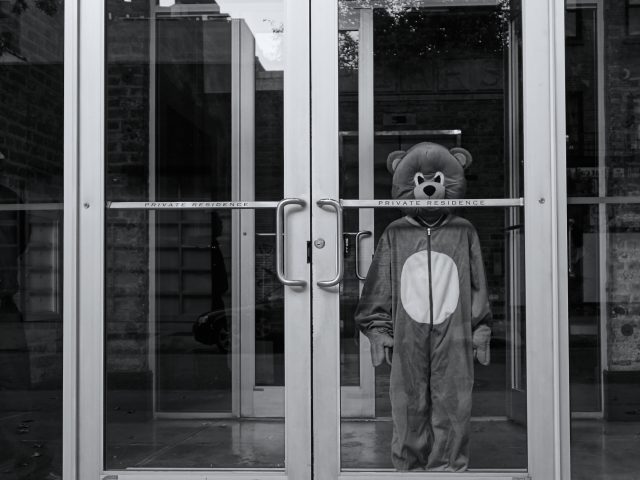 A black and white photograph of a child in costume standing at the entryway to a residence.