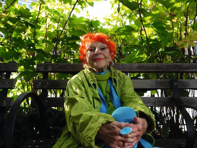 A colorful photograph of a smiling older woman in a park.