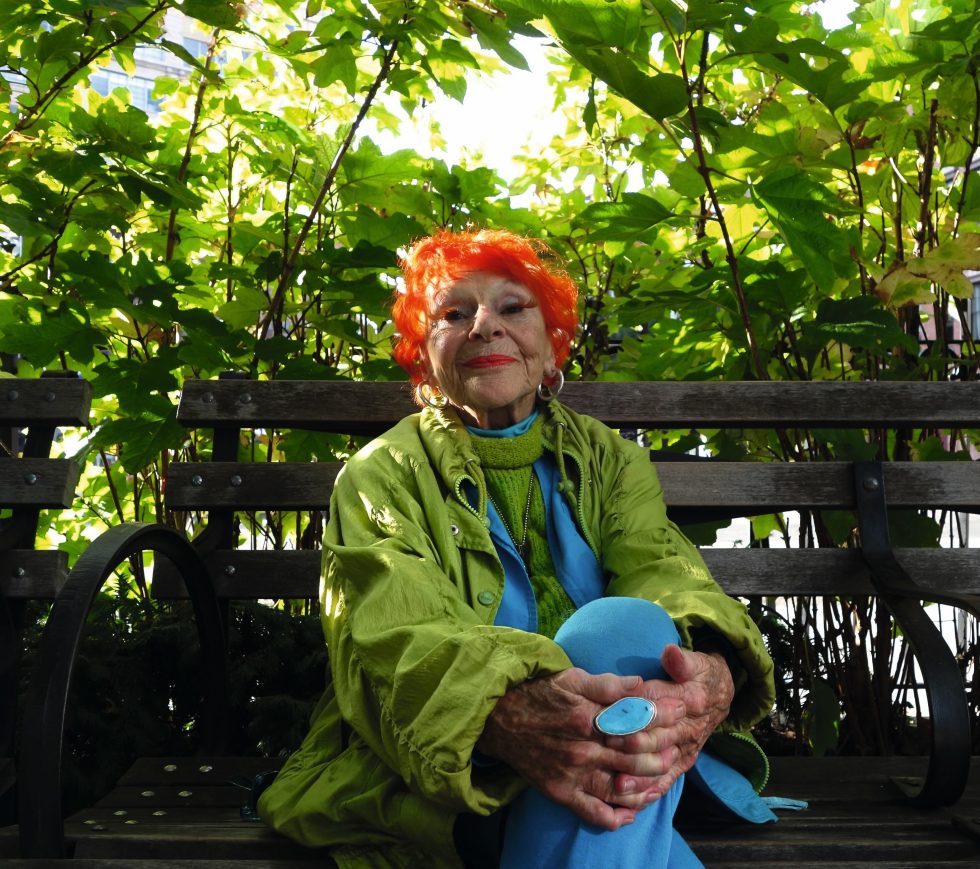 A colorful photograph of a smiling older woman in a park.