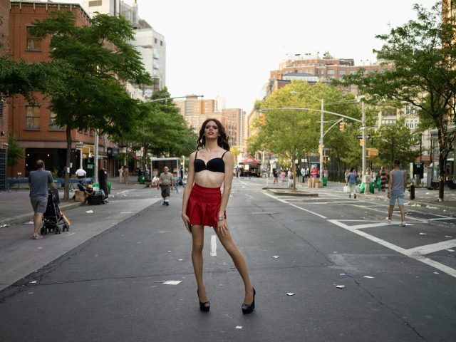A photograph of a woman in a red dress standing in the middle of a city street.