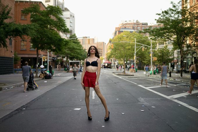 A photograph of a woman in a red dress standing in the middle of a city street.