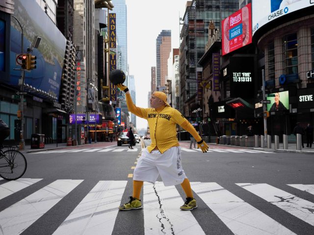 A color photograph of an older basketball played holding up a ball in Time's Square.