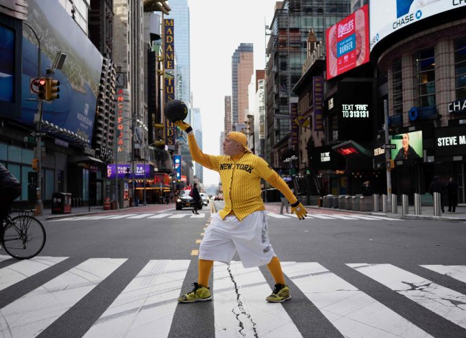 A color photograph of an older basketball played holding up a ball in Time's Square.