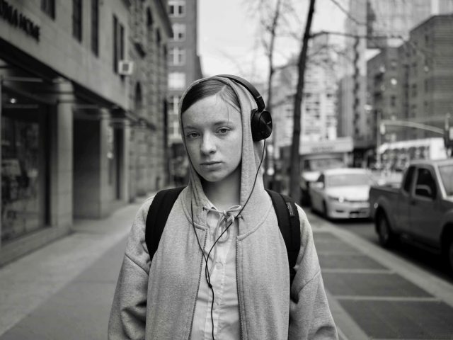 A black and white photograph of a person in a hoodie wearing over ear headphones on a city street