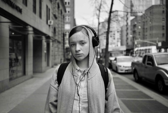 A black and white photograph of a person in a hoodie wearing over ear headphones on a city street
