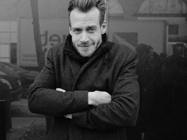 A black and white photograph of a man waiting to get into a fashion show.