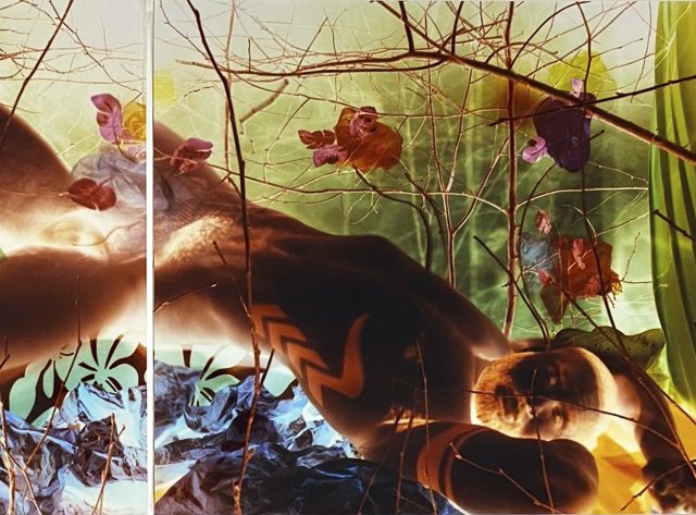 An intense colorful image of a man reclining in the nude among intricate set design.
