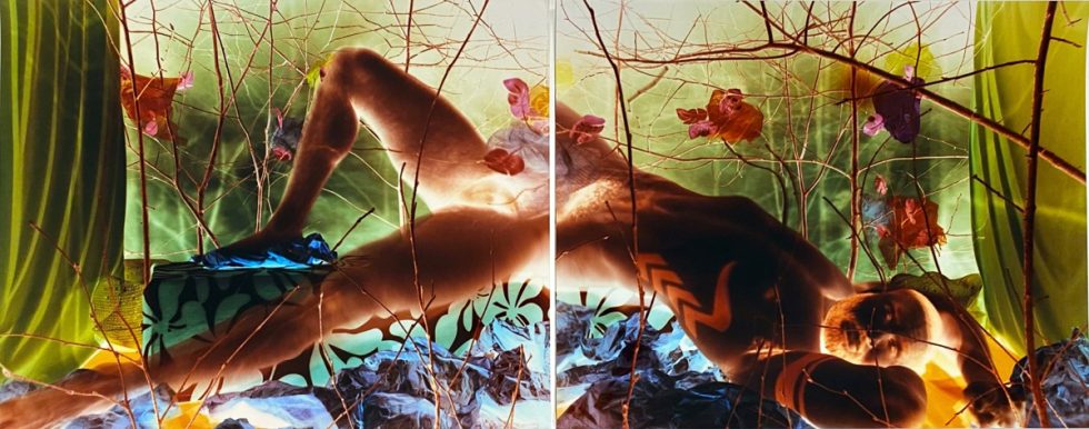 An intense colorful image of a man reclining in the nude among intricate set design.