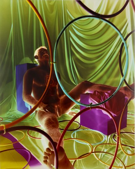 A colorful image of a nude man sitting on the floor with circles creating a design on top of the image.