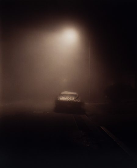 A moody image of a car at night in fog under a streetlight.