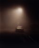 A moody image of a car at night in fog under a streetlight.