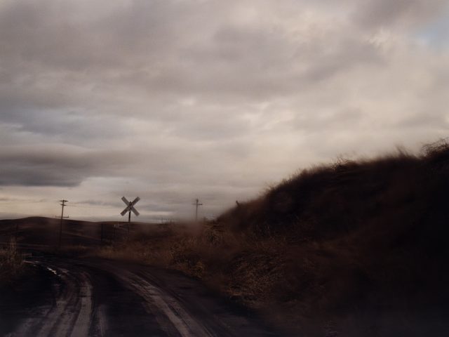 A landscape photograph of a dark road and hill with a cloudy sky.