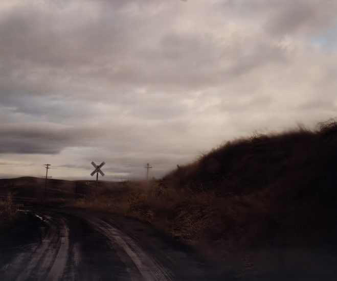 A landscape photograph of a dark road and hill with a cloudy sky.