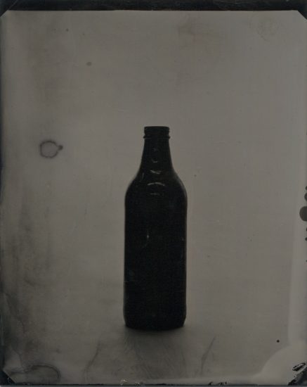 A black and white photograph of an empty glass beer bottle.