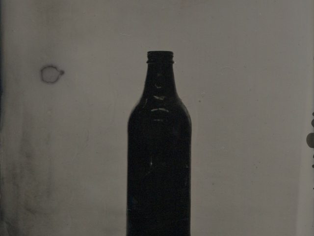 A black and white photograph of an empty glass beer bottle.