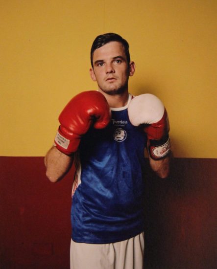 A photograph of a man in a blue tee shirt with boxing gloves.