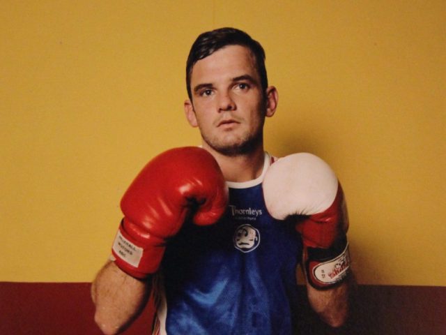 A photograph of a man in a blue tee shirt with boxing gloves.