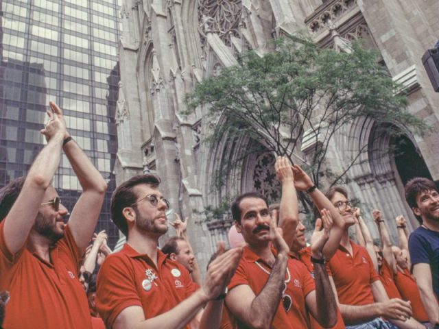 A group of men in red shirts march beside a large church.