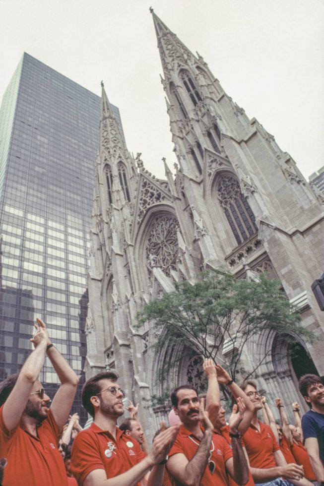 A group of men in red shirts march beside a large church.