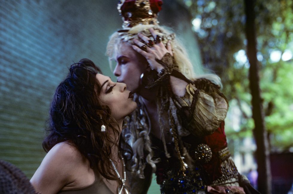 A color photograph of two people kissing on the cheek in elaborate costumes.