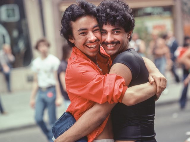 A photograph of two men embracing on a city sidewalk.