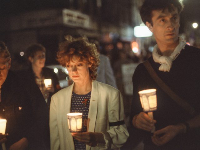 A color photograph of three individuals holding candles at a vigil/march for AIDS victims.
