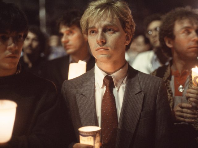 A young man in a suit holds a candle in honor of AIDS victims in the 80s.
