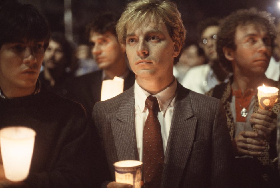 A young man in a suit holds a candle in honor of AIDS victims in the 80s.