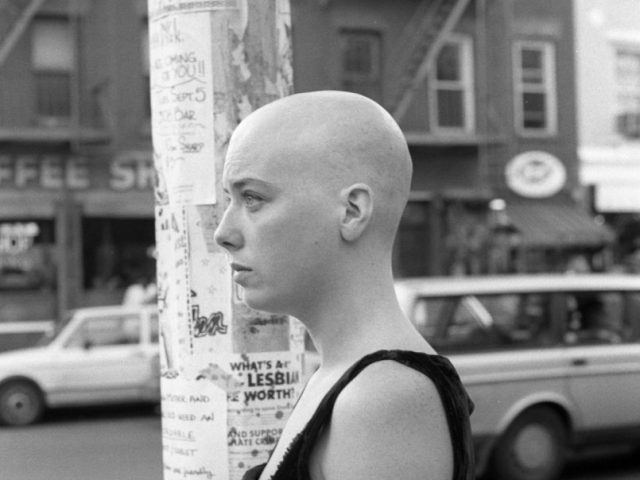 A black and white photograph of a person with a bald head standing next to a light pole.