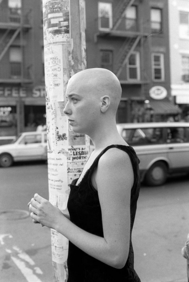 A black and white photograph of a person with a bald head standing next to a light pole.
