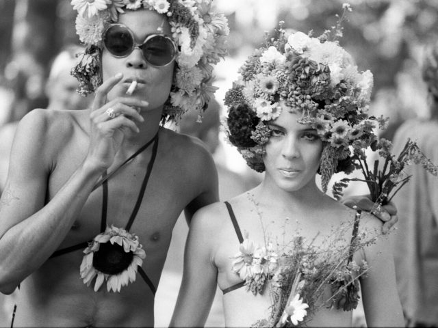 A black and white photograph of two people in floral costumes smoking cigarettes.