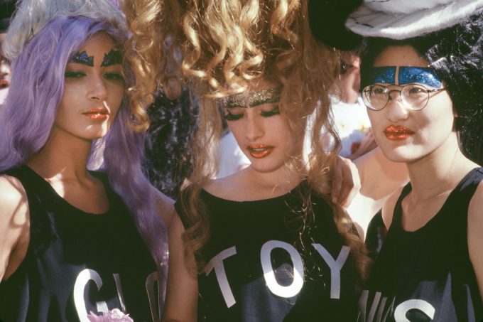 A photograph of a group of three people in black tee shirts and wigs.