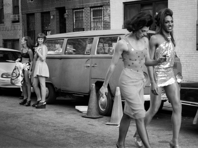 A black and white photograph of a scene of fashionable people handing out on a city street.
