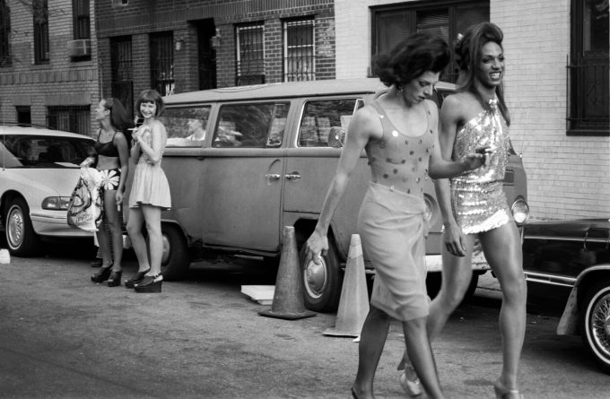 A black and white photograph of a scene of fashionable people handing out on a city street.