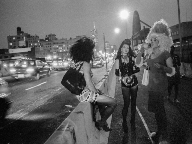 A black and white photograph of a group of people standing beside a highway at night.