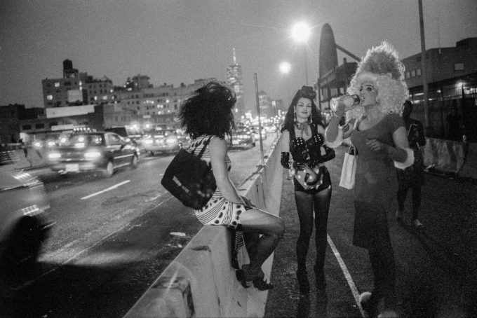 A black and white photograph of a group of people standing beside a highway at night.
