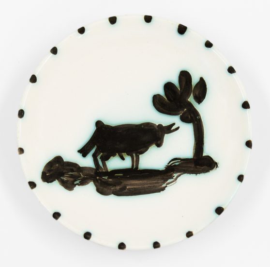 A photograph of a ceramic plate with a bull standing under a tree.