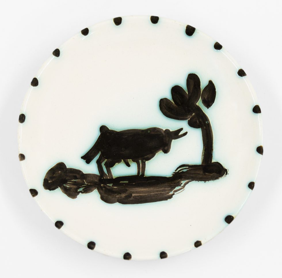 A photograph of a ceramic plate with a bull standing under a tree.