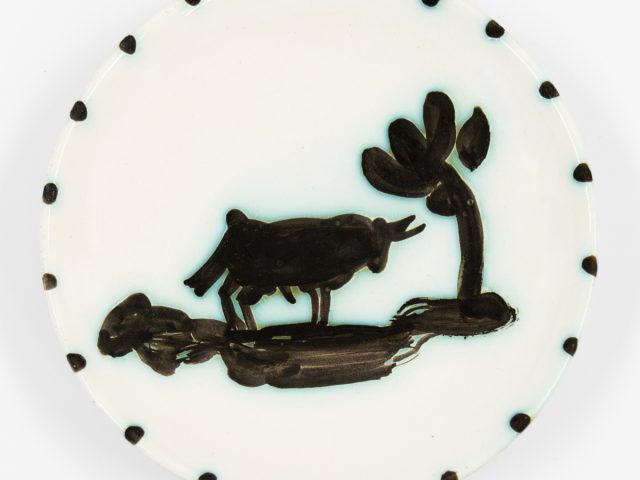 A photograph of a ceramic plate with a bull standing under a tree.