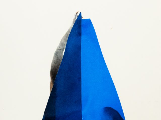 A photograph of a blue triangle in a white gallery or studio setting.