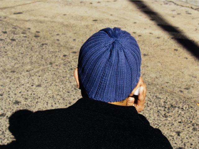 A photograph of the back of a person's head wearing a blue beanie holding a cell phone.