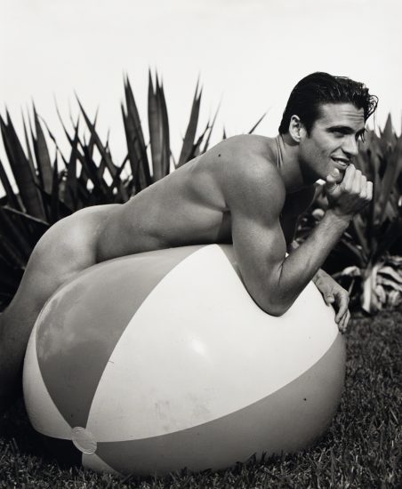 A black and white photograph of a nude man on a large inflatable beach ball.
